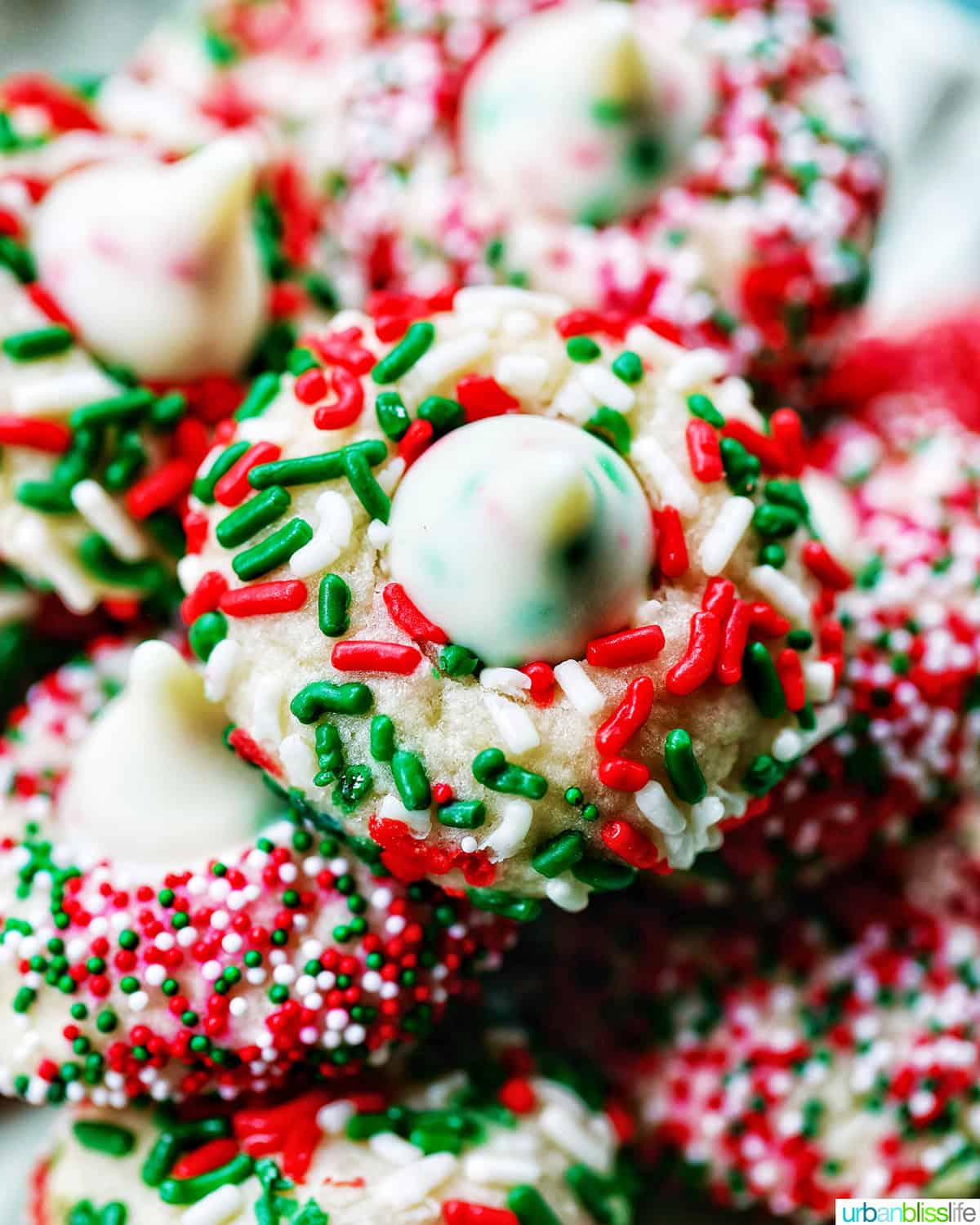 almond Christmas cookies with red and green sprinkles stacked on a plate.