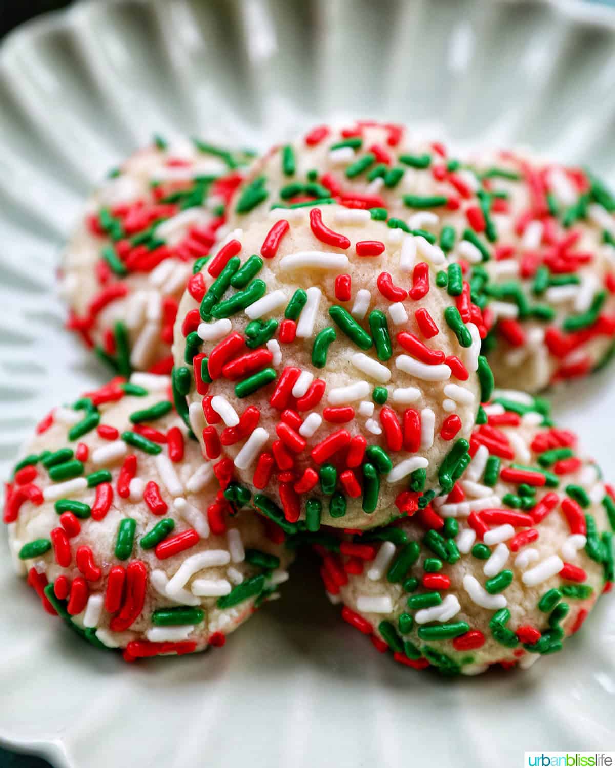 almond Christmas cookies with red and green sprinkles stacked on a plate.