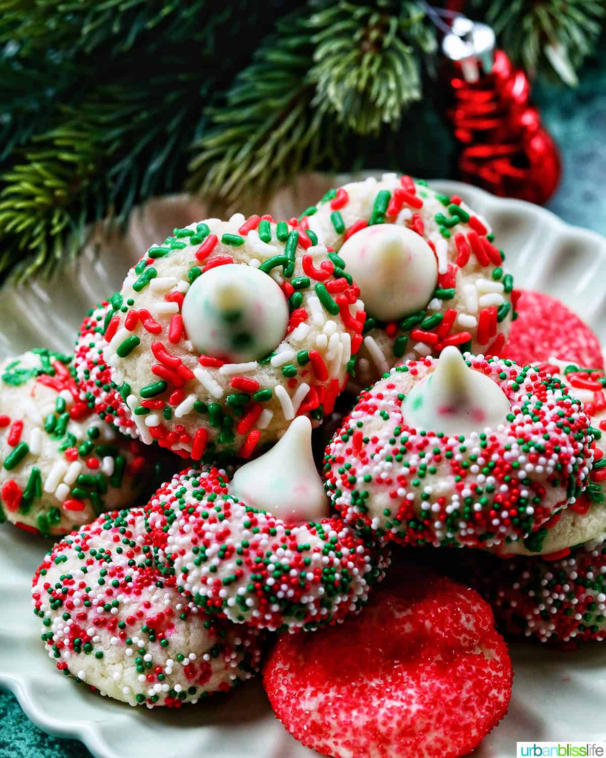 almond Christmas cookies with red and green sprinkles stacked on a plate.