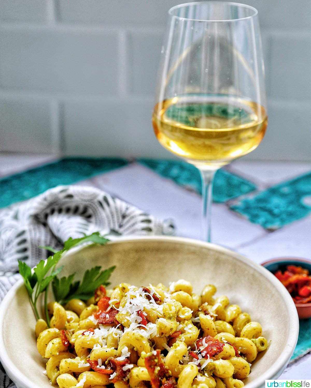 bowl of bacon pesto pasta with glass of white wine.