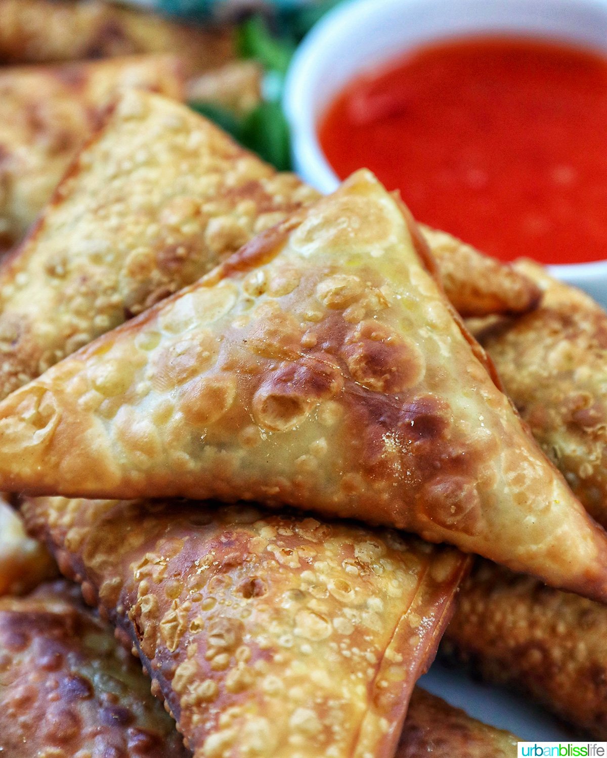 plate full of vegan curry samosas with a side of sweet chili dipping sauce and herb garnish.