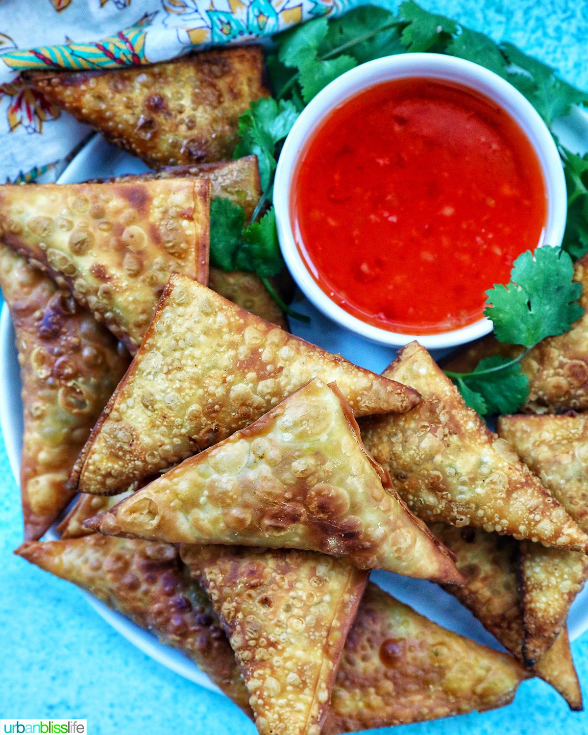 plate full of vegan curry samosas with a side of sweet chili dipping sauce and herb garnish.