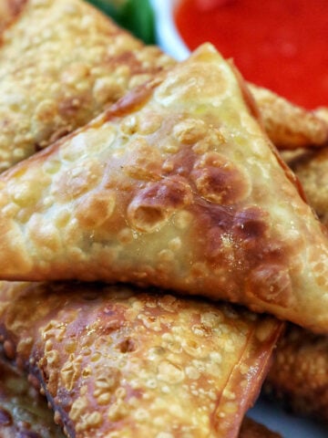 plate full of vegan curry samosas with a side of sweet chili dipping sauce and herb garnish.