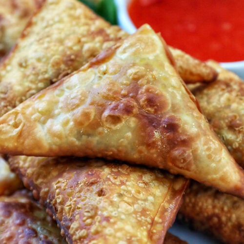 plate full of vegan curry samosas with a side of sweet chili dipping sauce and herb garnish.