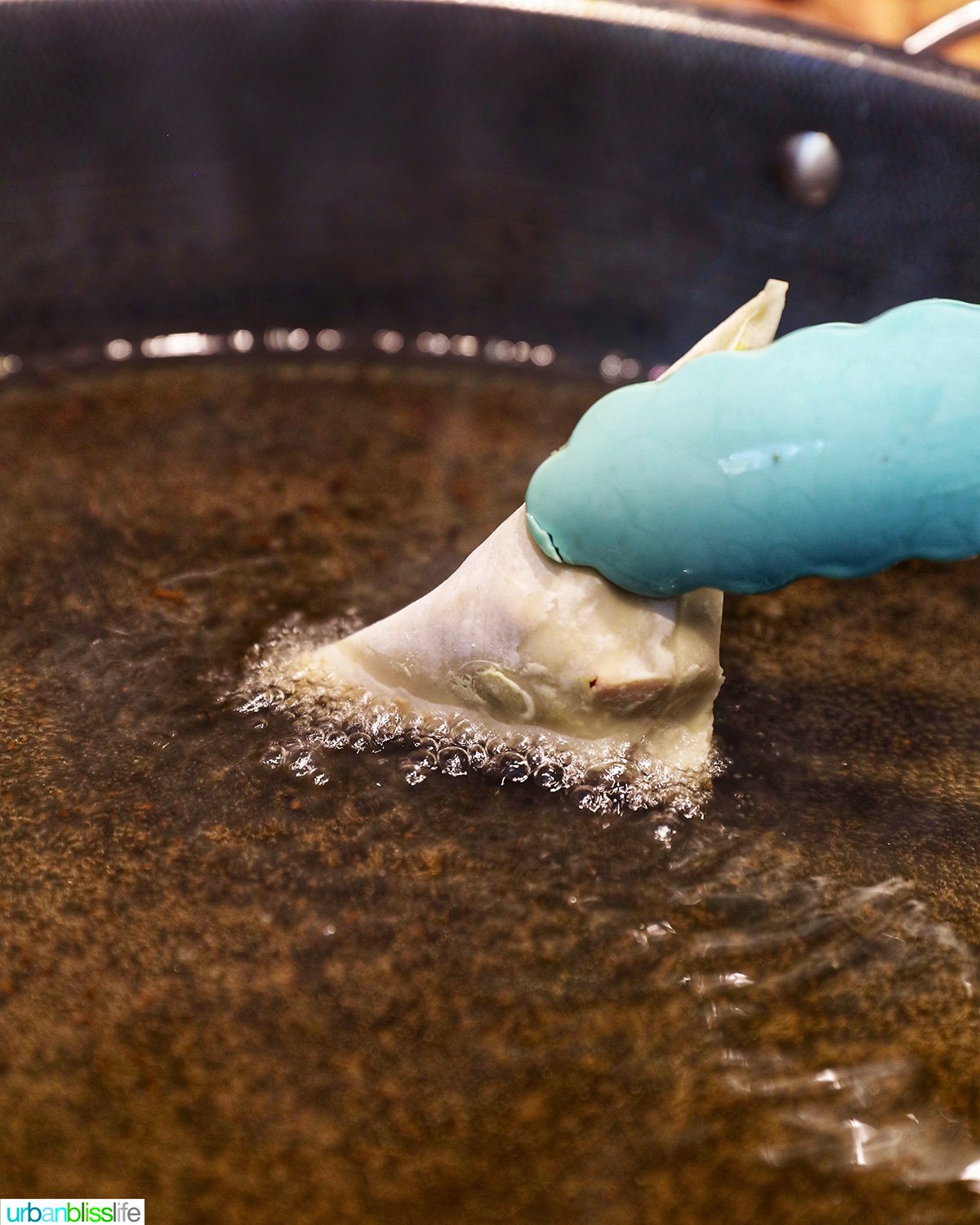 tongs dipping one side of a samosa into hot oil.