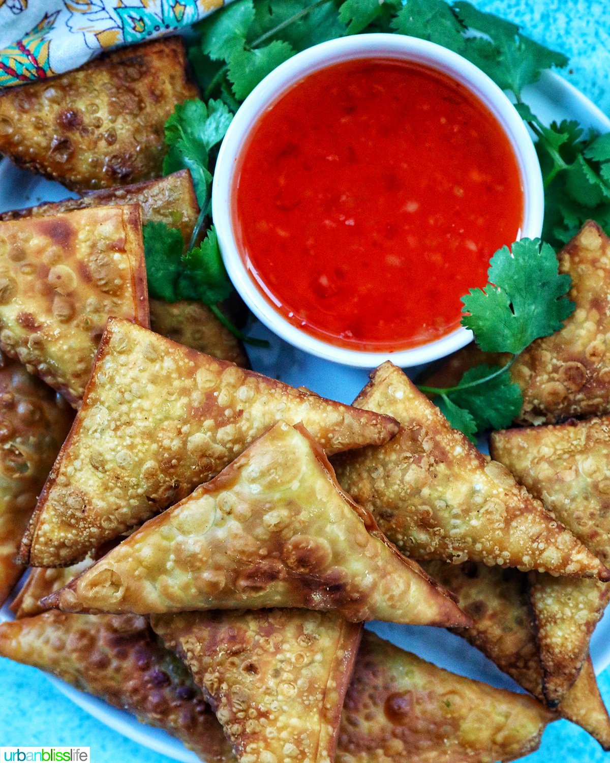 plate full of vegan curry samosas with a side of sweet chili dipping sauce and herb garnish.