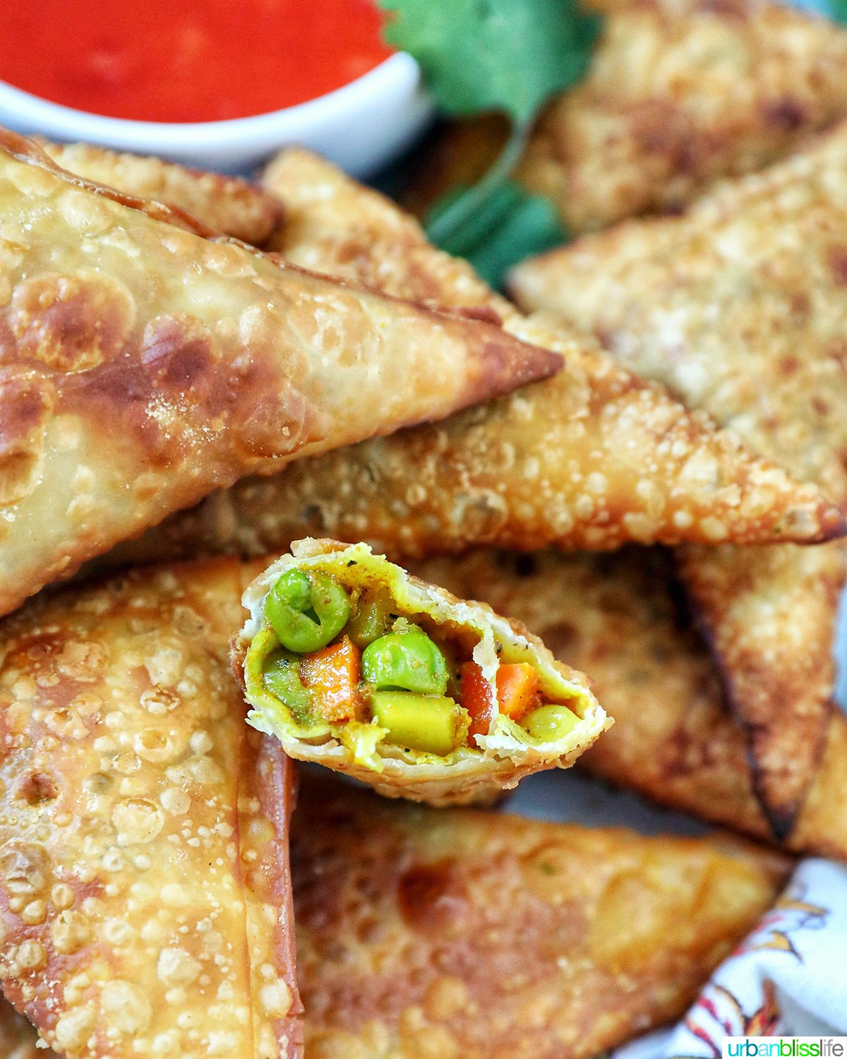 plate full of vegan curry samosas with a side of sweet chili dipping sauce and herb garnish and one cut open so you can see inside.