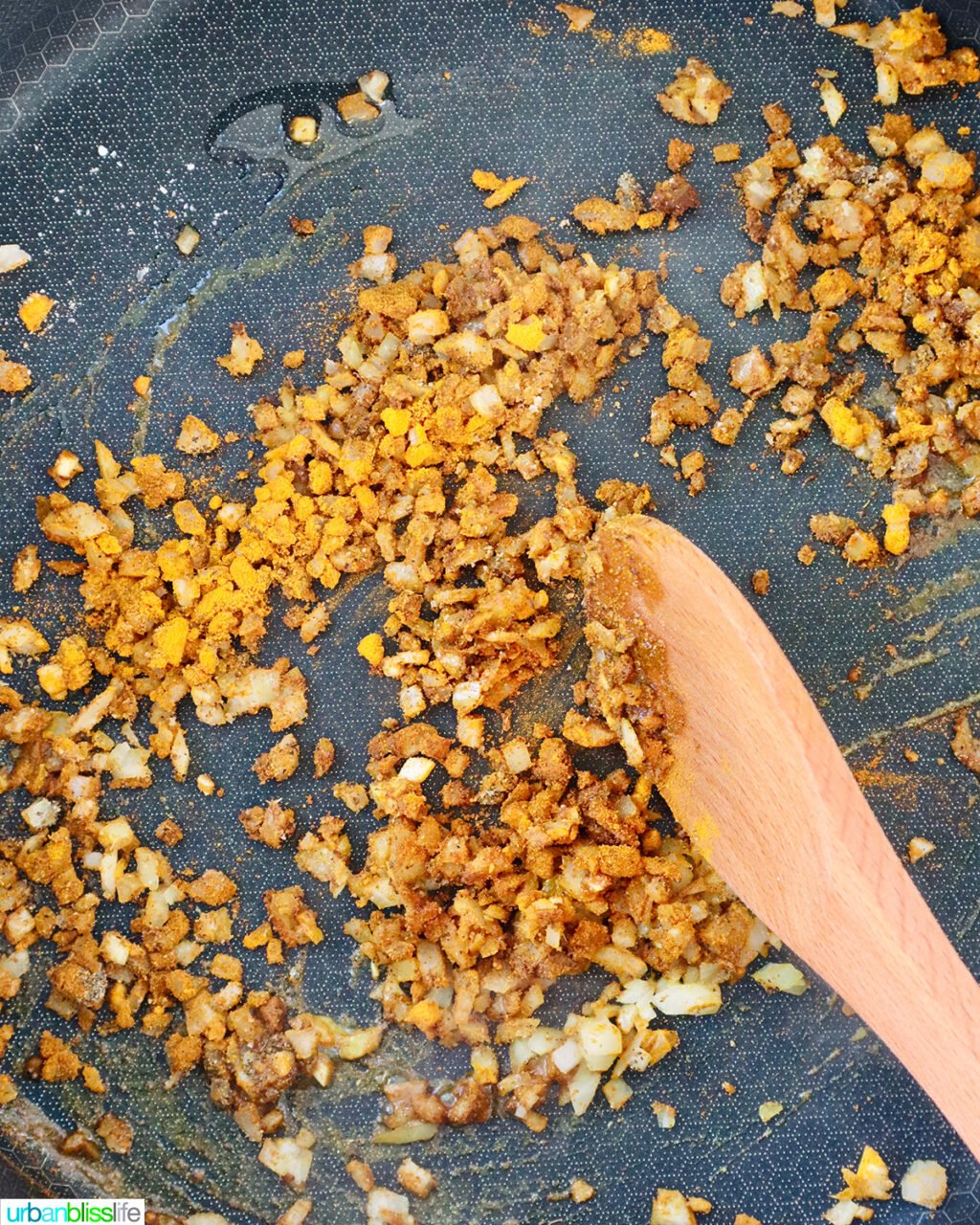 wooden spoon stirring curry spices and garlic in a pan.