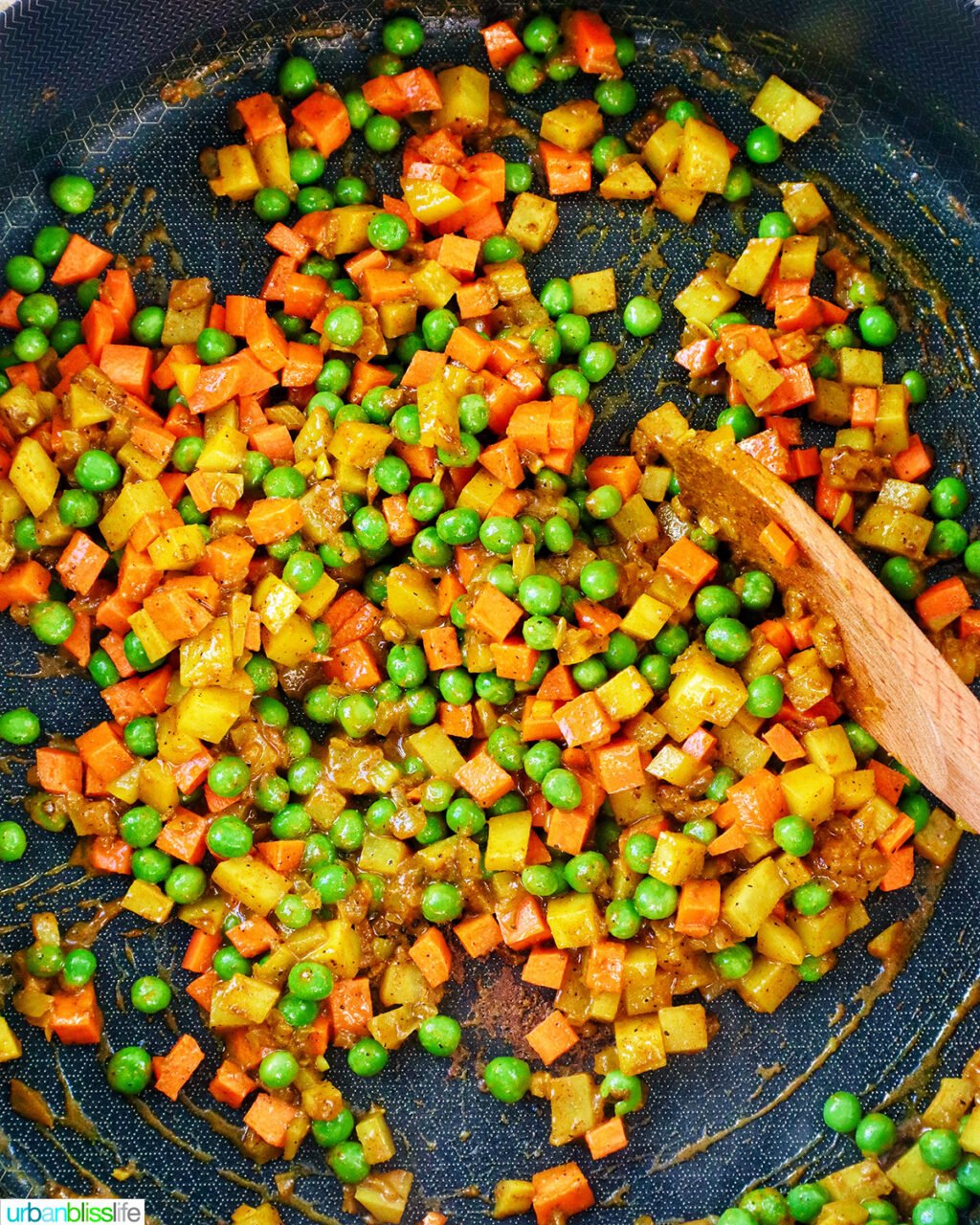 peas, carrots added to potatoes and curry spices in a pan.