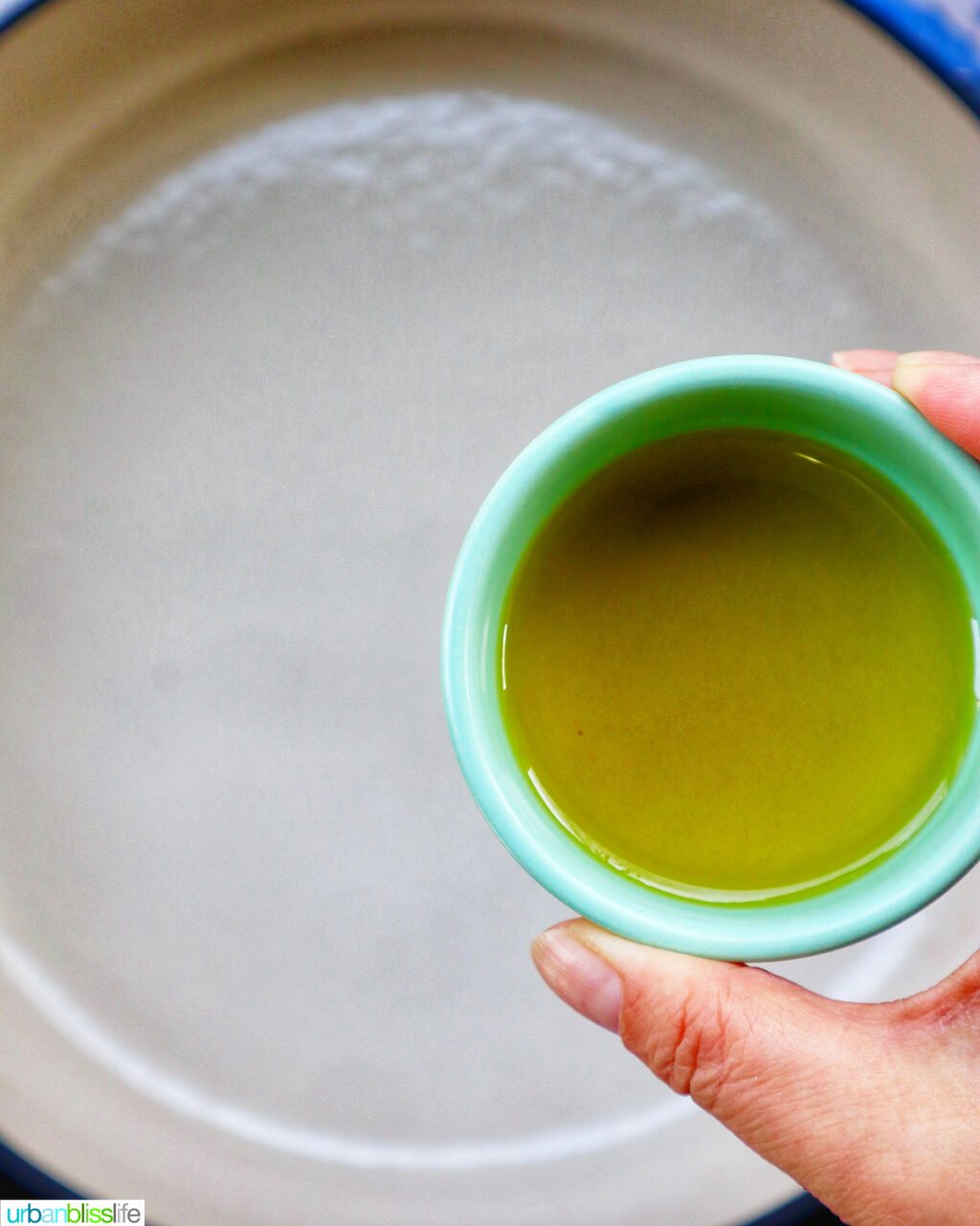 hand holding bowl of olive oil over a pan.