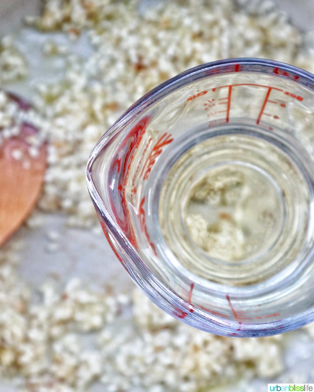 measuring cup of white wine over a pan of risotto.