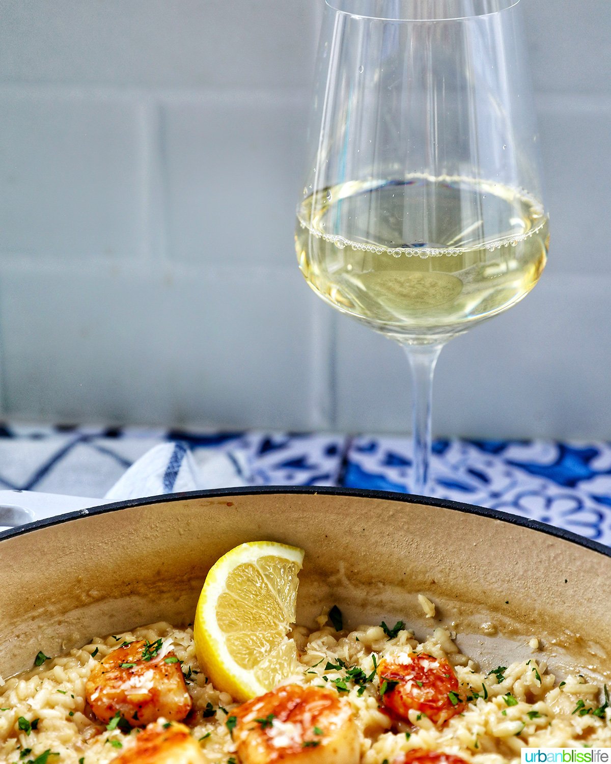 braising pan with scallop risotto with lemon wedge and parsley garnish with glass of white wine.