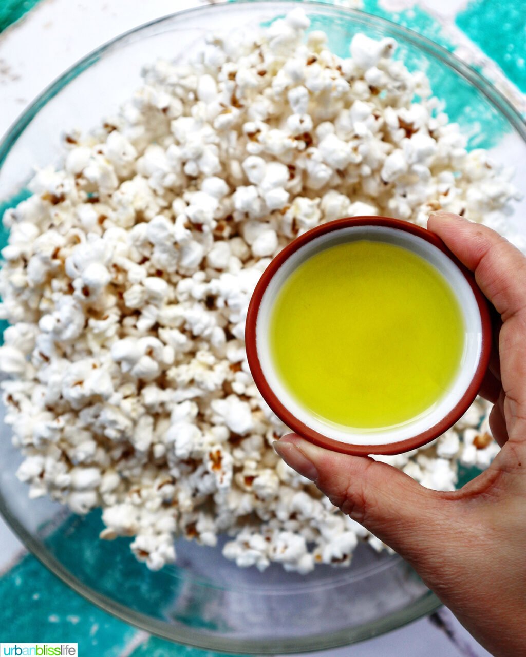 hand holding a bowl of pickle juice over a bowl of popcorn.