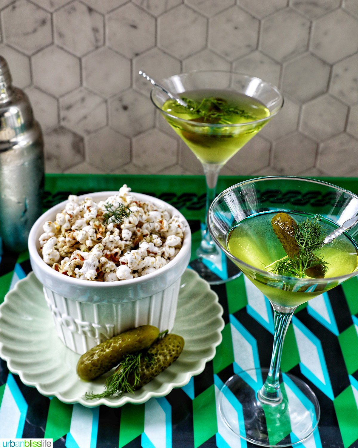 two dill pickle martinis next to a bowl of of dill pickle popcorn.