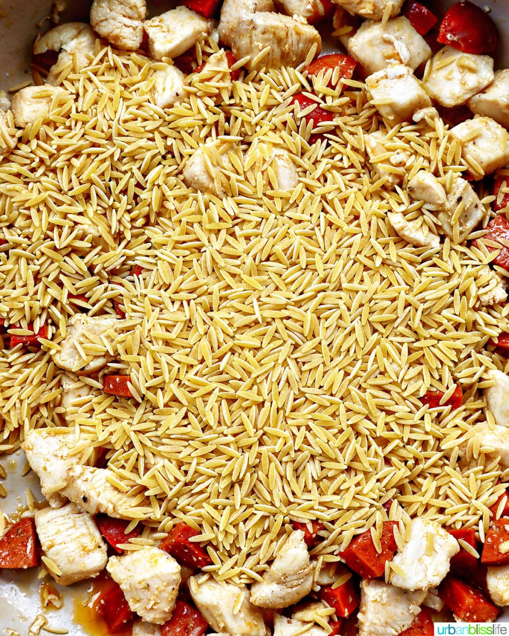 orzo added to a pan of chicken and chorizo.