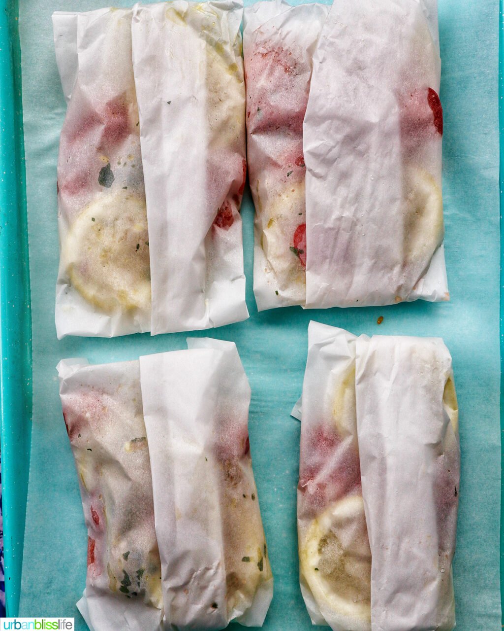 Cod en Papillote, four wrapped on a blue baking sheet.