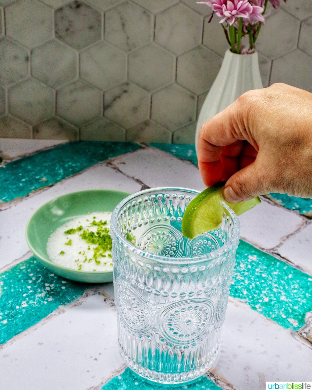 hand with slice of lime on a cocktail glass rim.