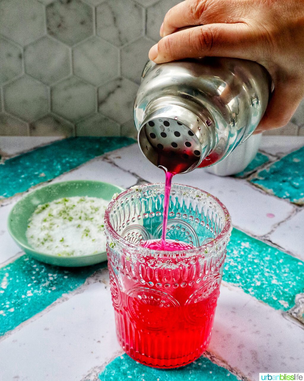 pouring a prickly pear margarita from a cocktail shaker into a glass.