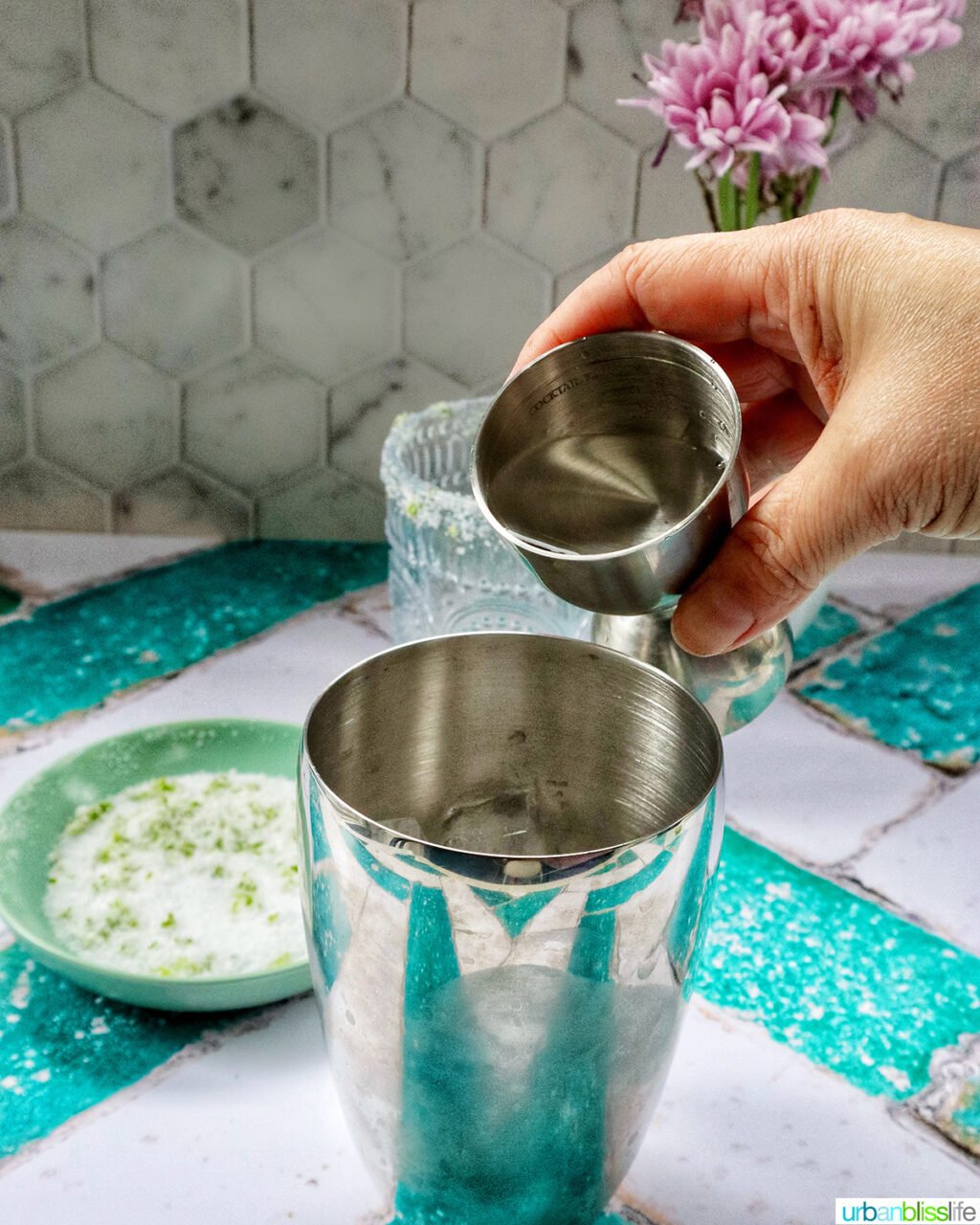 hand pouring liquid into a cocktail shaker.