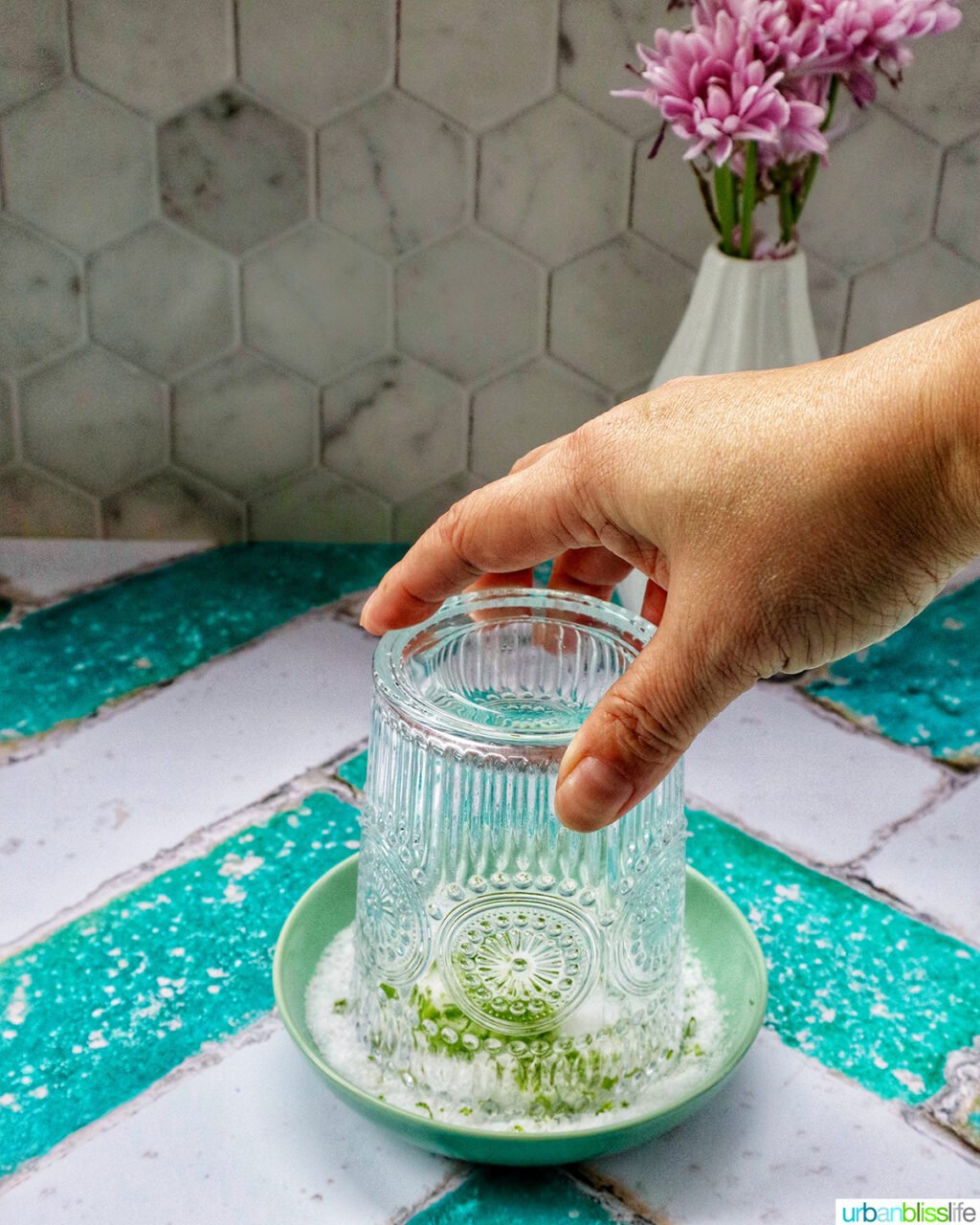 hand holding a cocktail glass over a shallow bowl of lime salt.