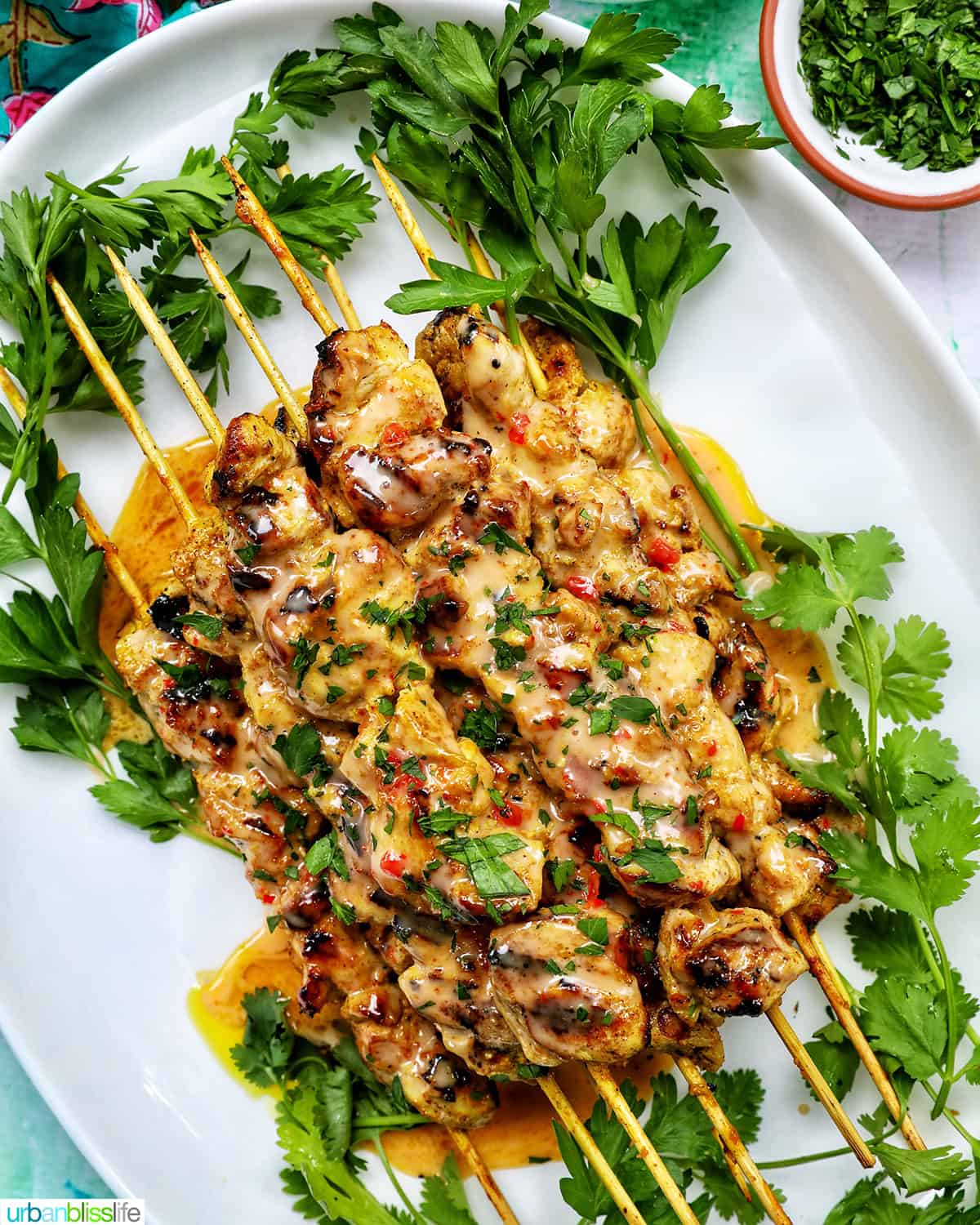 bang bang chicken skewers on a plate with herb garnish.