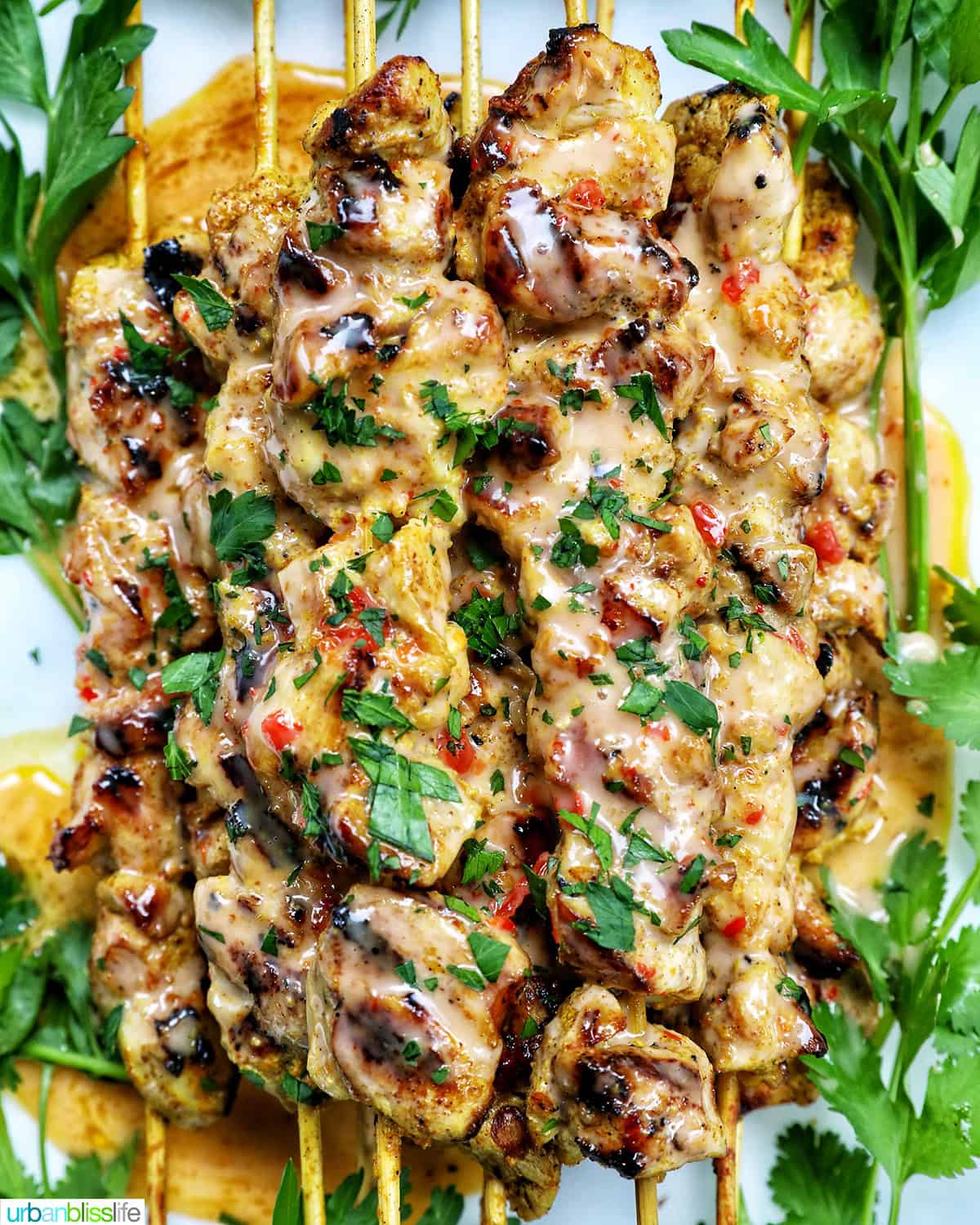 bang bang chicken skewers on a plate with herb garnish.