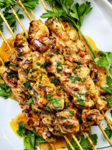bang bang chicken skewers on a plate with herb garnish.