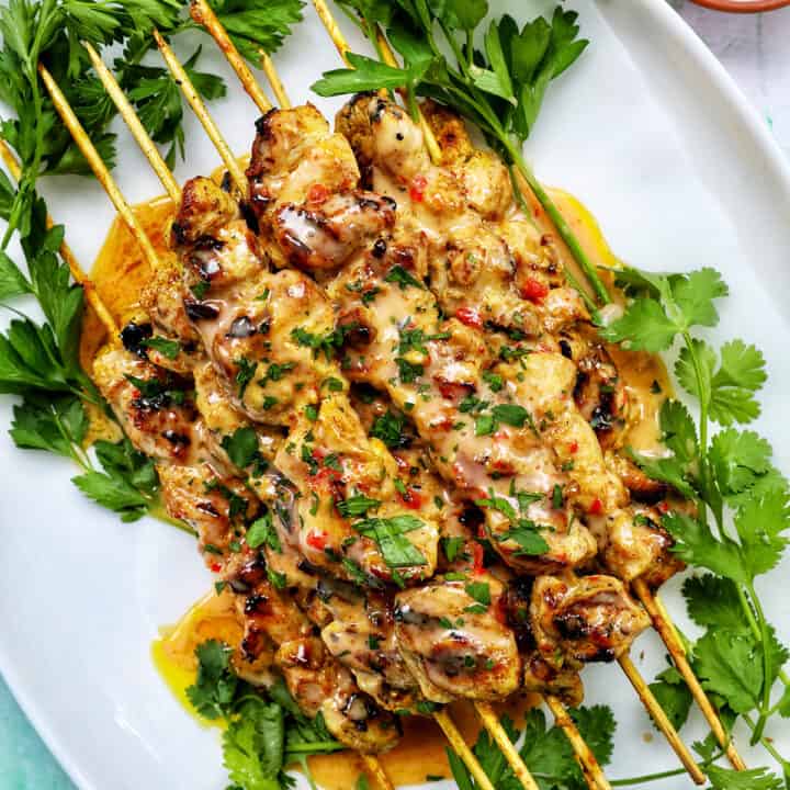 bang bang chicken skewers on a plate with herb garnish.