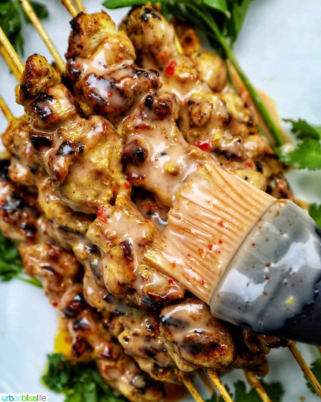 brushing bang bang sauce on chicken skewers.