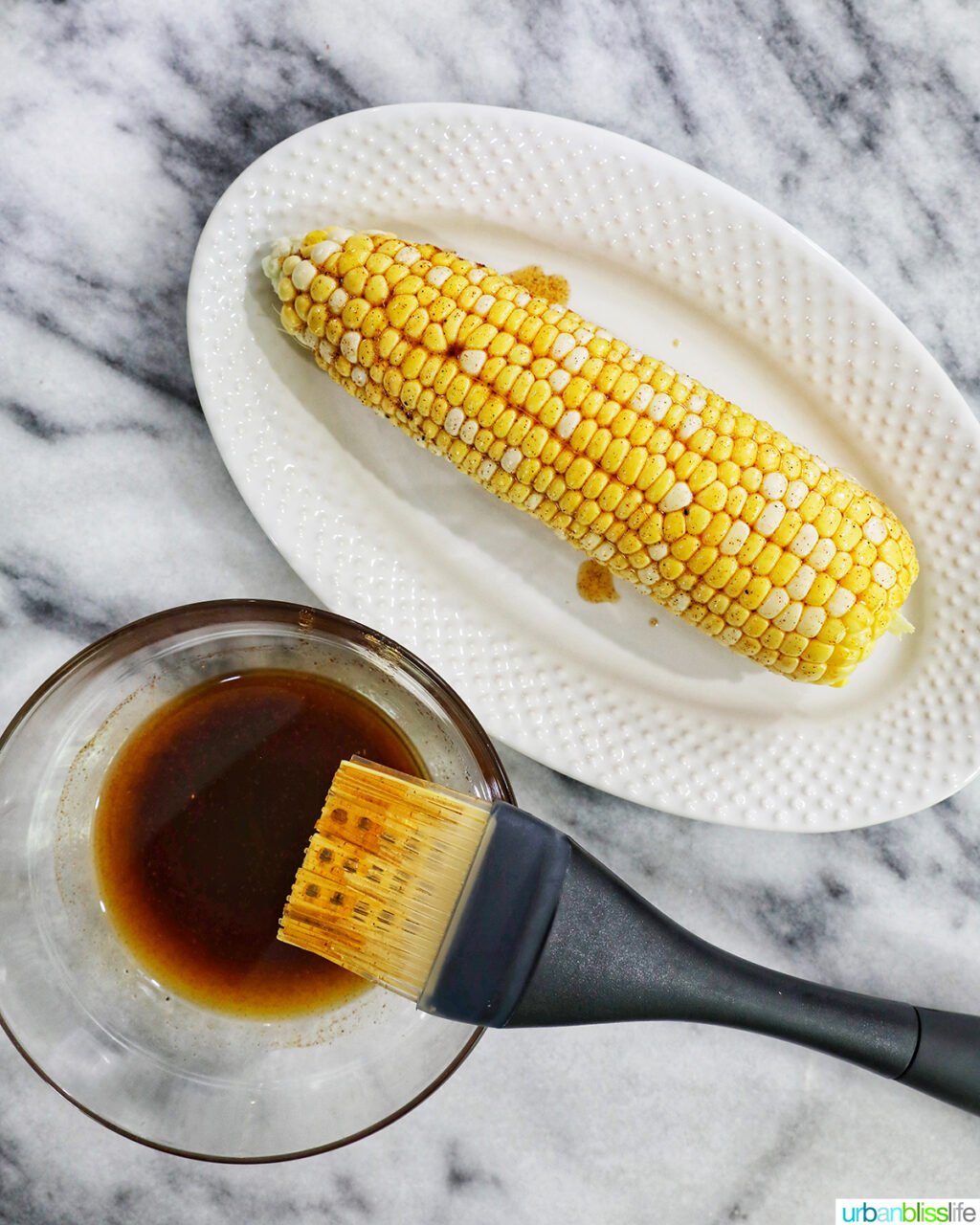 basting brush with marinade and corn on the cob.