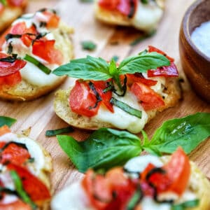 lots of crostini pizzas on a wooden board with a side bowl of salt.
