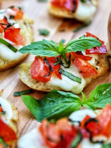 lots of crostini pizzas on a wooden board with a side bowl of salt.