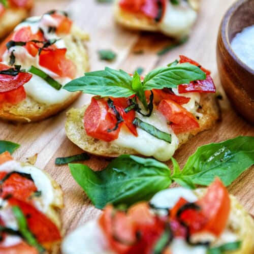 lots of crostini pizzas on a wooden board with a side bowl of salt.