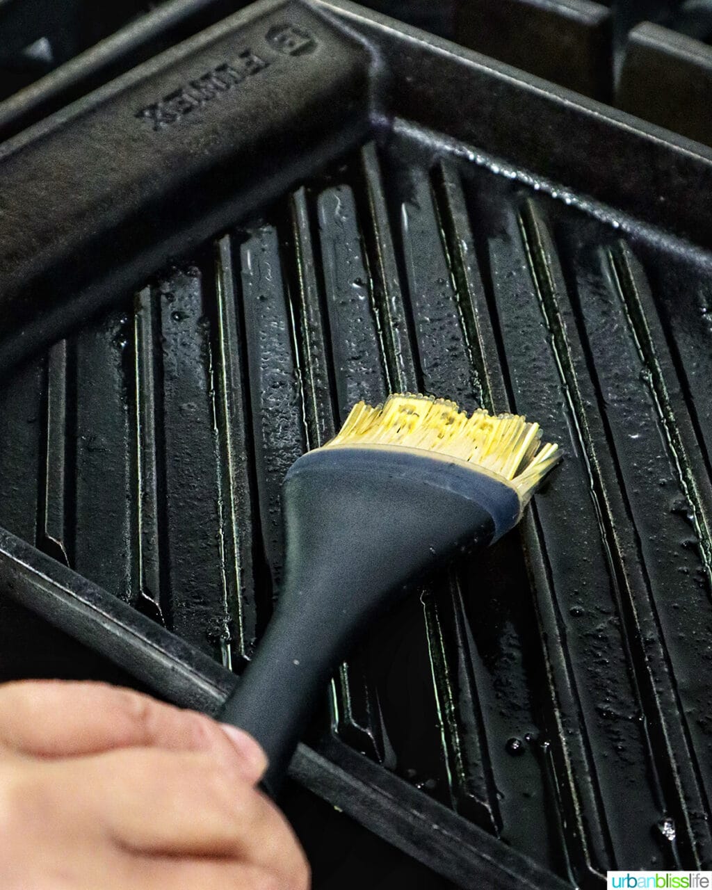 hand brushing oil onto a grill pan.