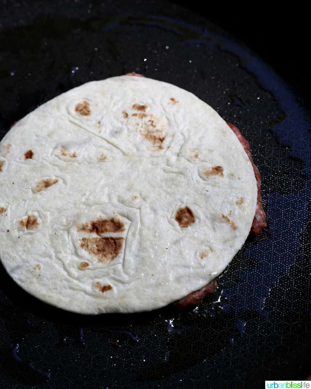 smash burger on a taco tortilla turned over on a skillet.