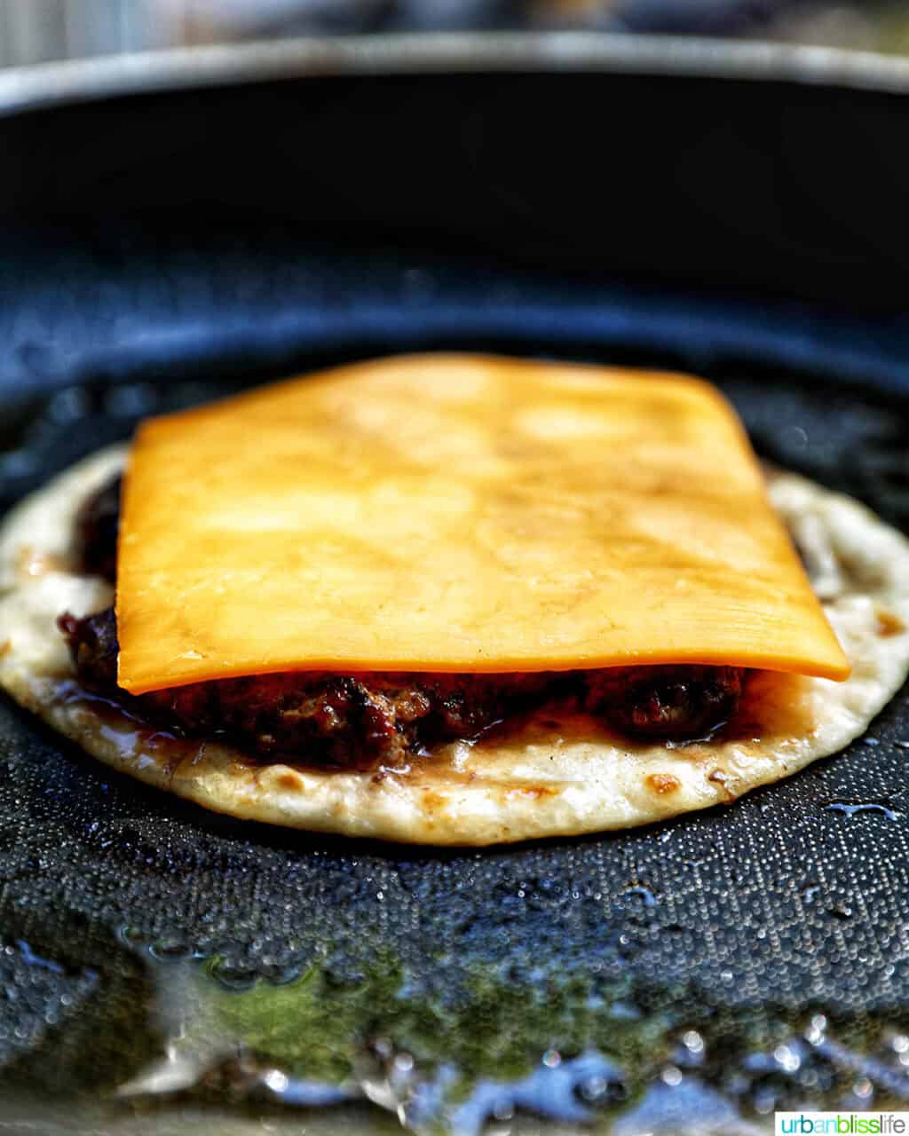 cheese slice on top of a smash burger on a taco tortilla.