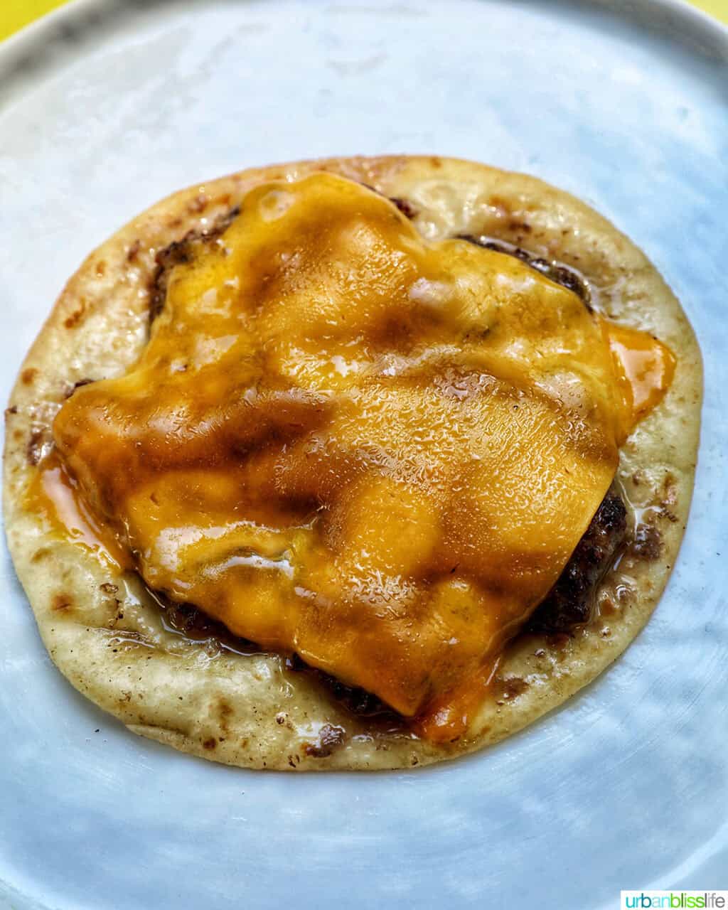 cheese slice on top of a smash burger on a taco tortilla.