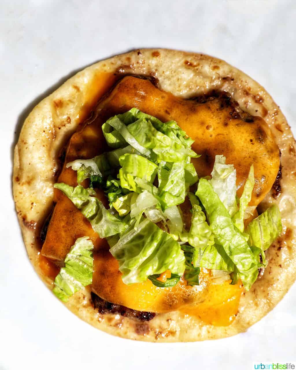 lettuce over cheese slice on top of a smash burger on a taco tortilla.