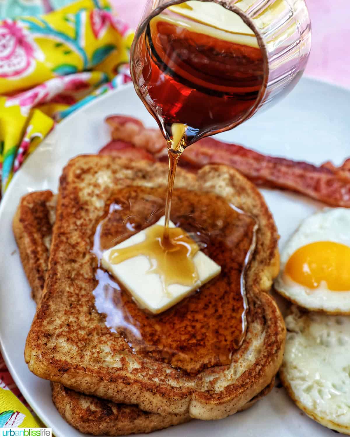 maple syrup pouring over a stack of high protein french toast with bacon and eggs.