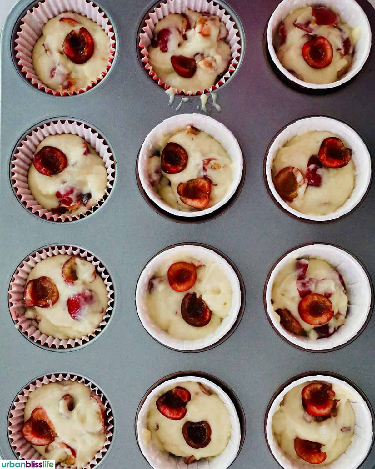cherry muffin batter in muffin cups in a muffin tin.
