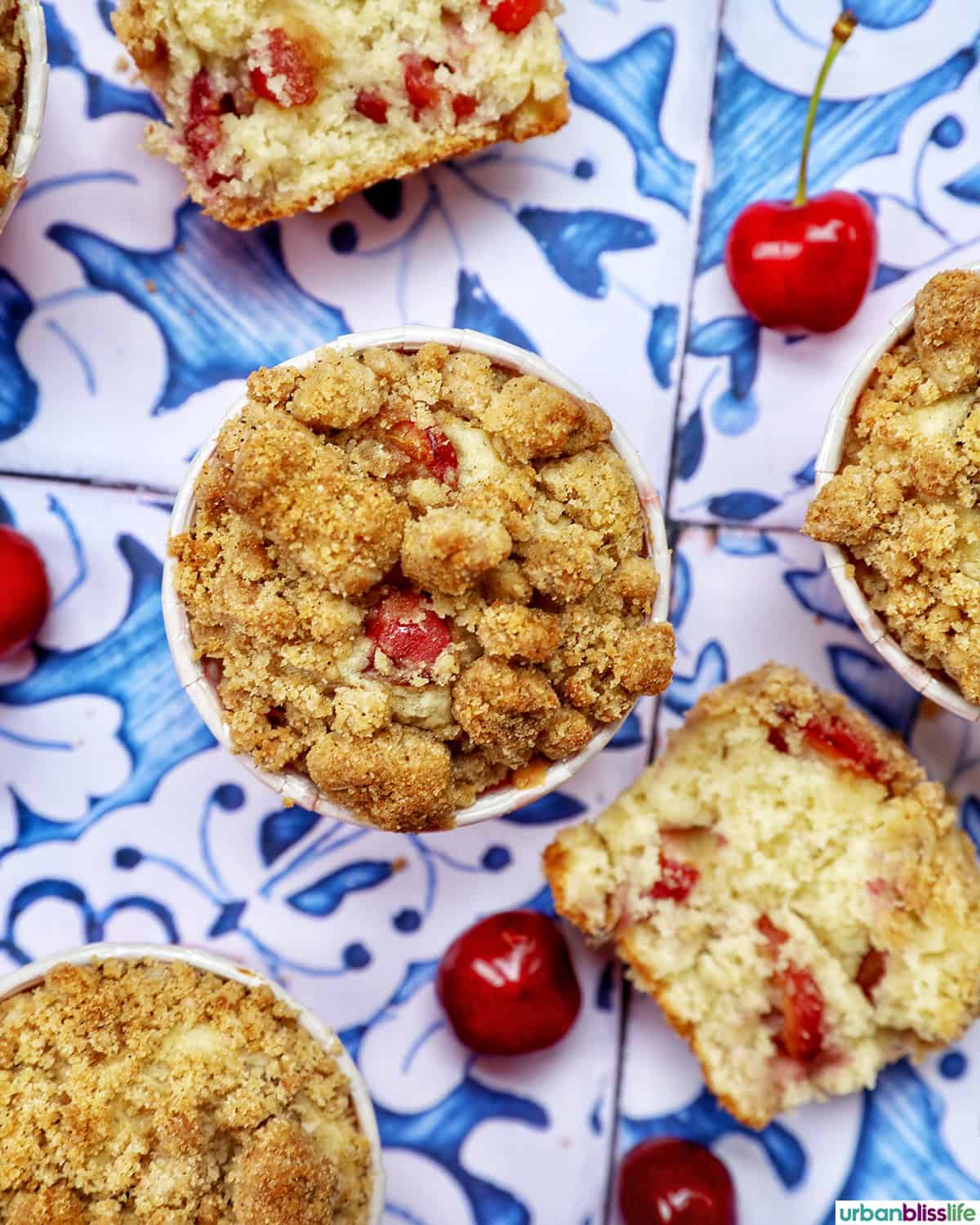 stack of cherry muffins with fresh cherries on a blue and white table.