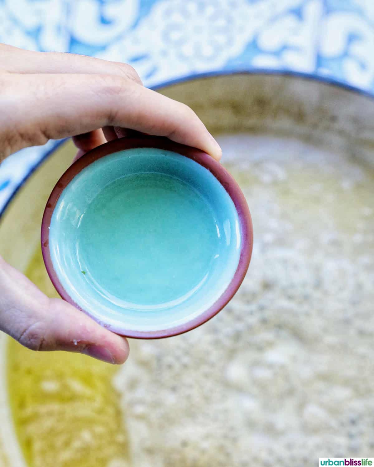 hand holding a small bowl of liquid over a pan.