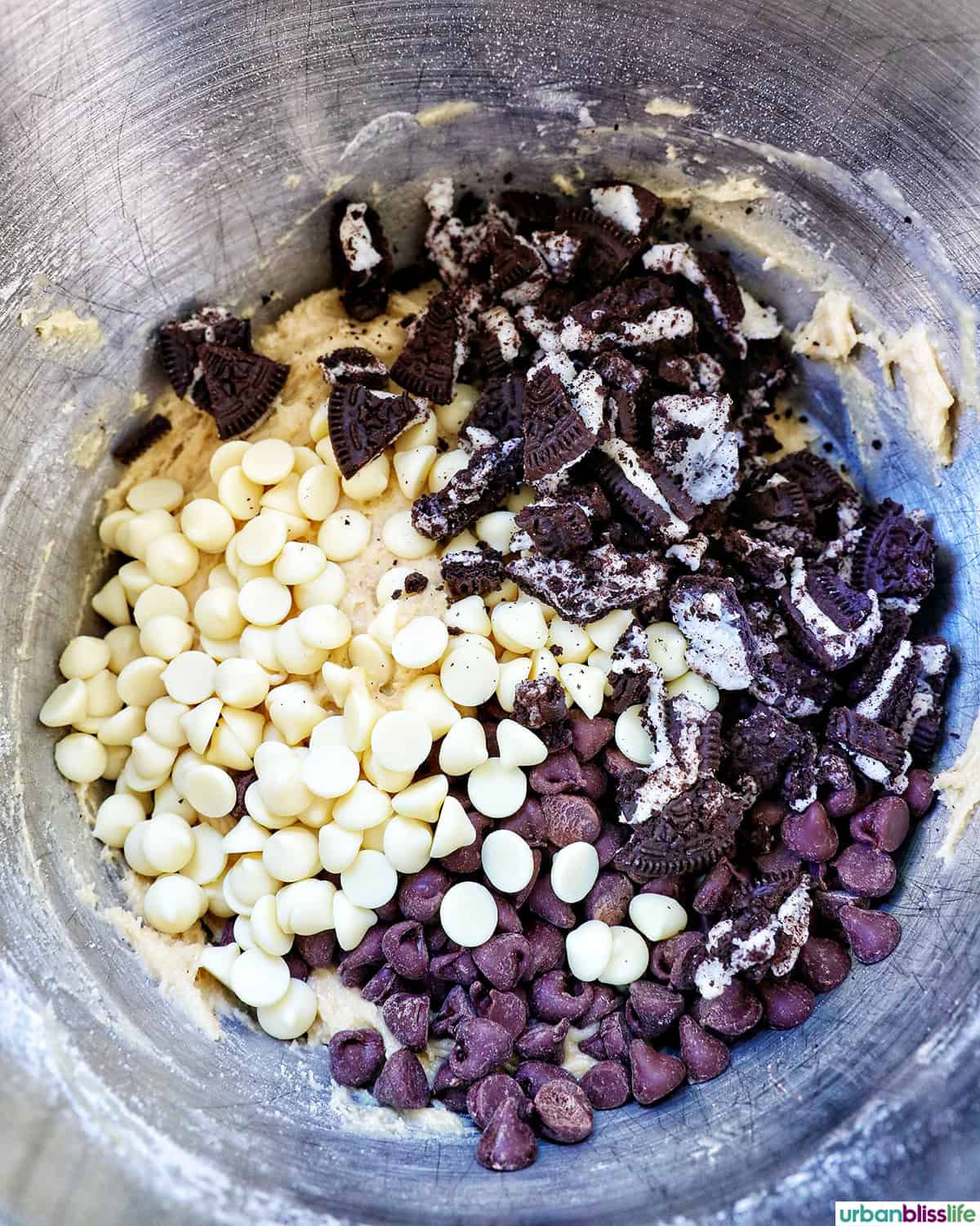 chocolate chips and Oreo cookies added to a stainless steel mixing bowl.