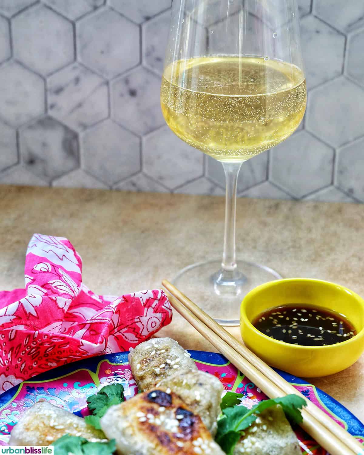 glass of white wine with plate of rice paper dumplings and dipping sauce.