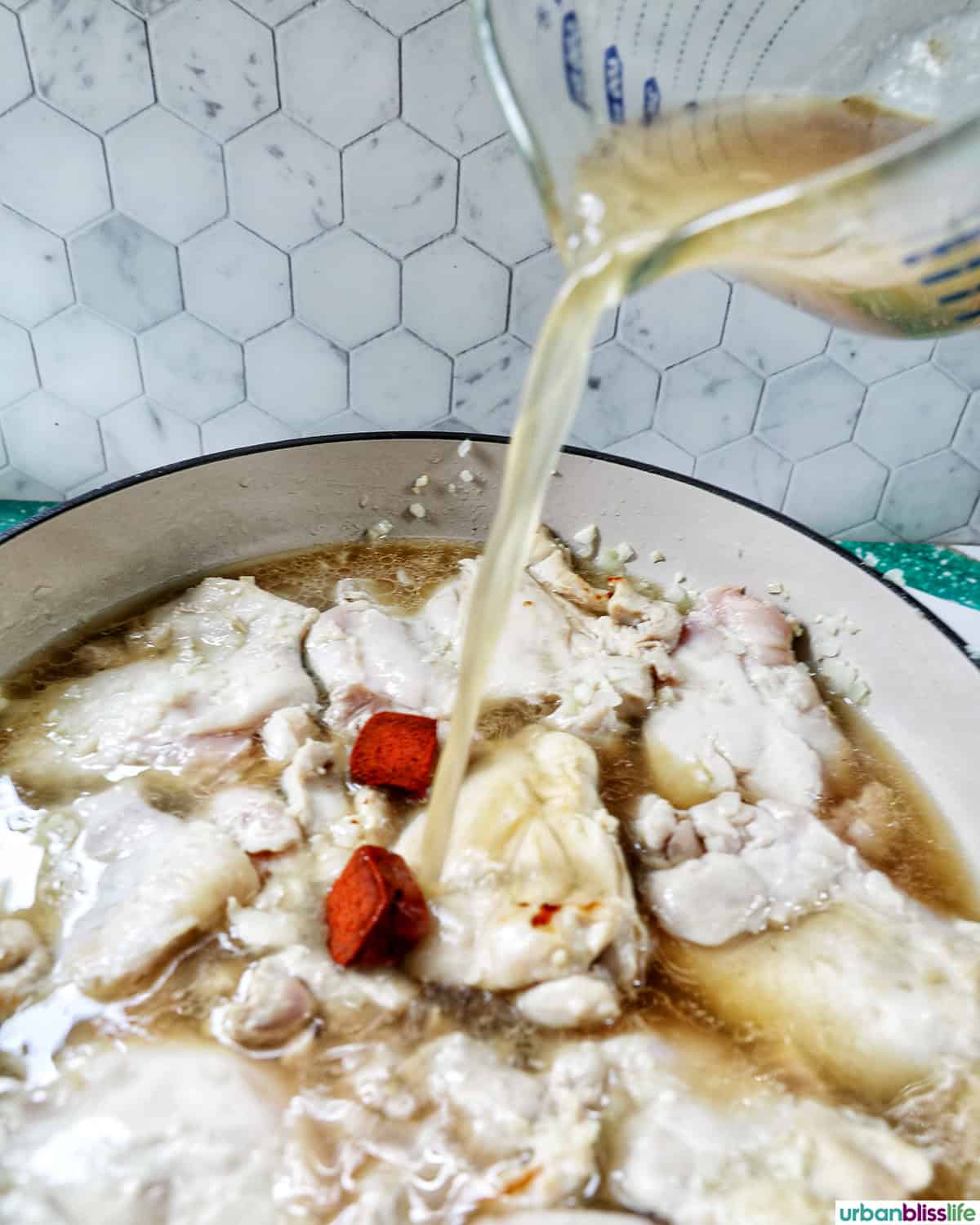 pouring chicken stock over chicken in a pan.