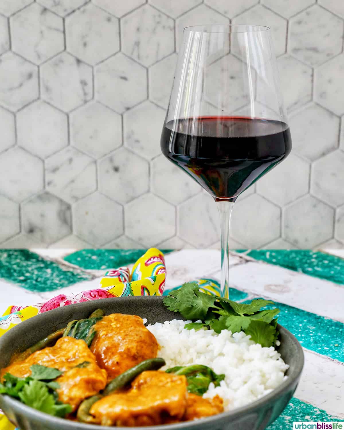 glass of red wine with plate of chicken kare kare and rice.