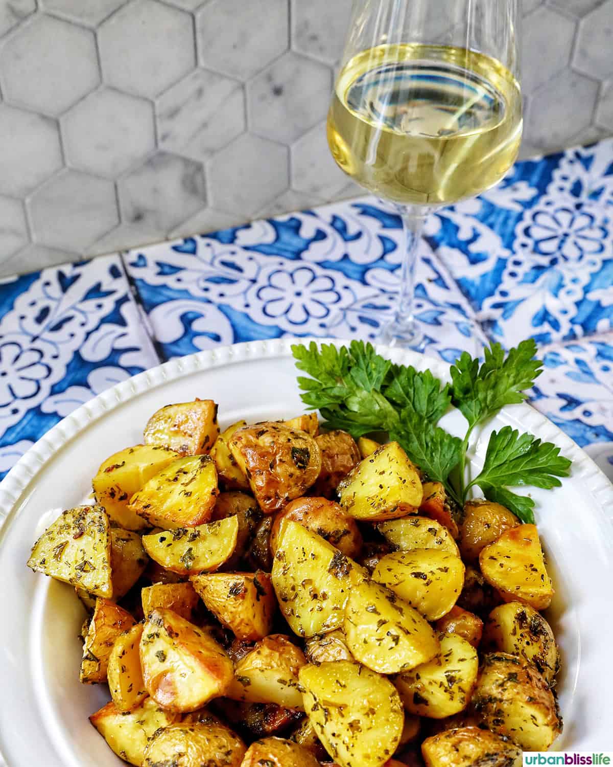 bowl of herby potatoes with glass of white wine.