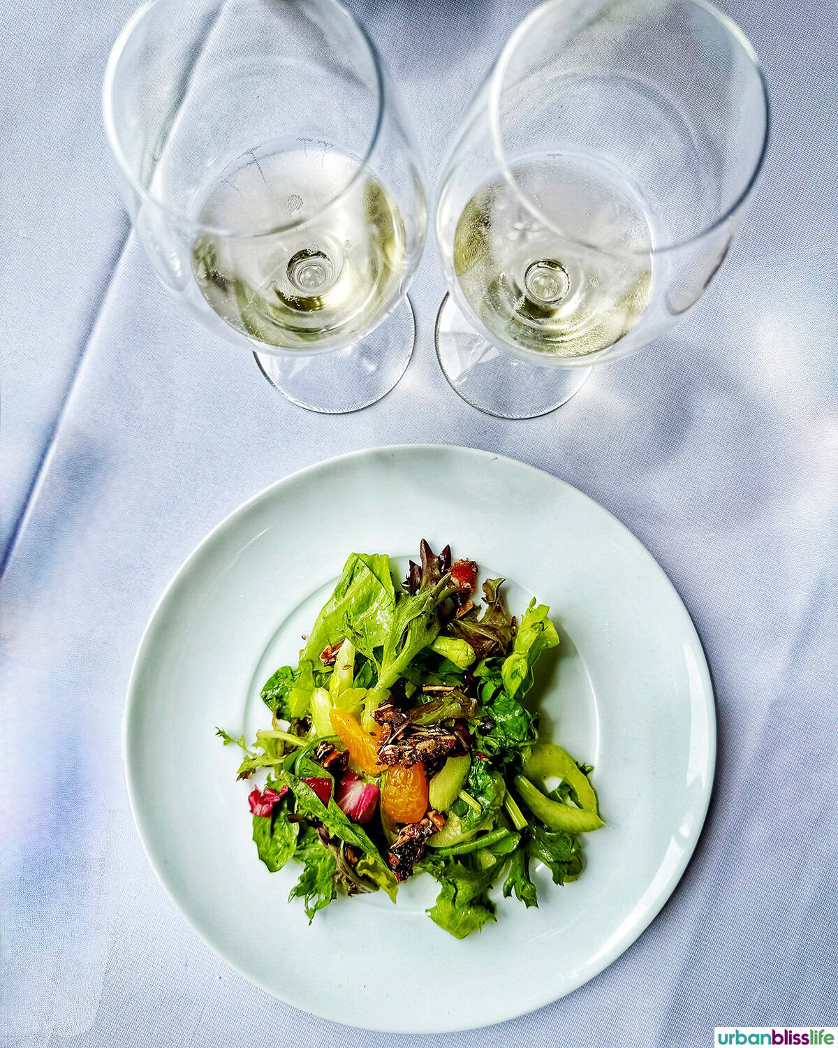 two glasses of sparkling wine by salad on a white plate.