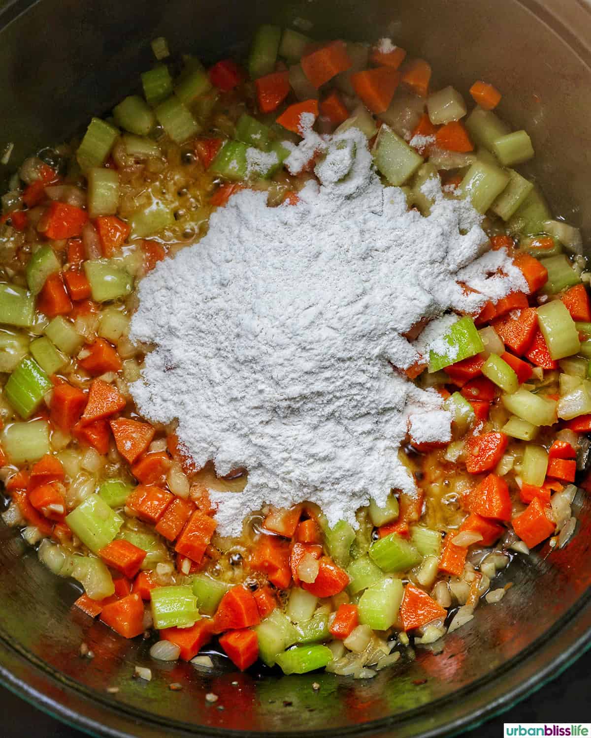 flour added to carrots, celery, garlic, onions cooking in a pot.