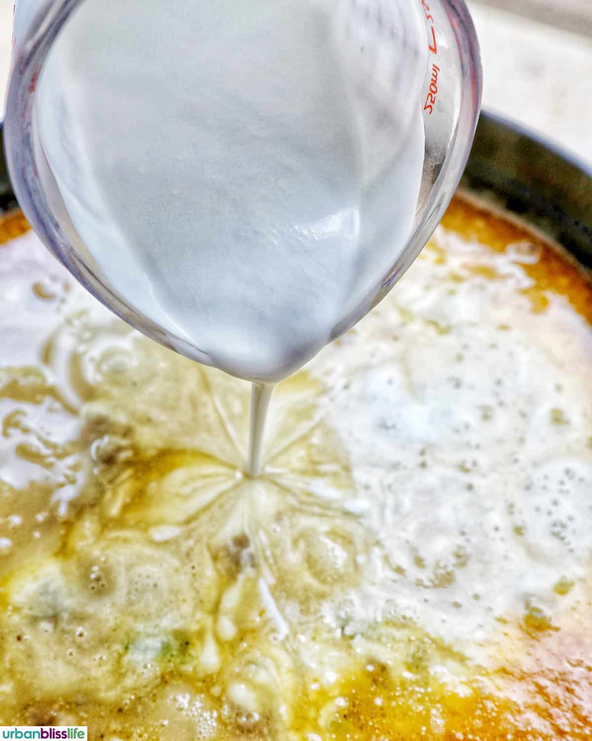 pouring cream into a carrots, celery, garlic, onions cooking in a pot.